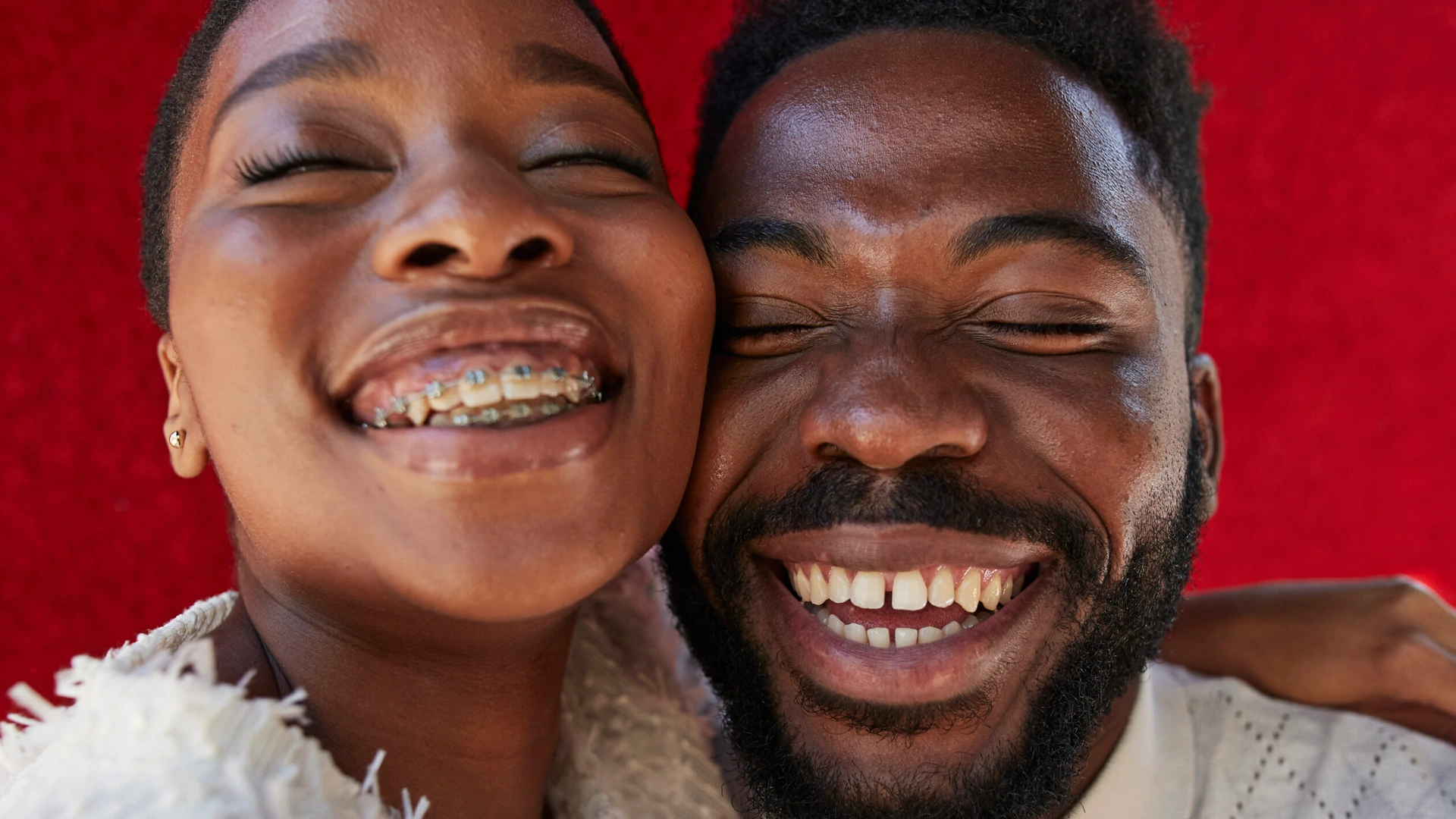 Smiling friends with eyes closed against red wall