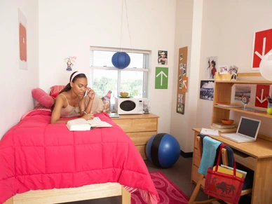Young woman using mobile phone on bed in dorm room