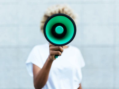 Front view of an afro american woman shouting through a megaphone while standing outdoors on the street.