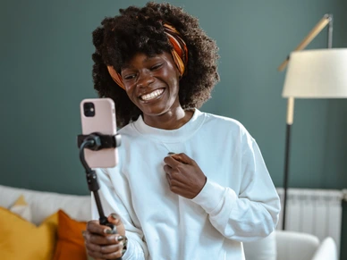Joyful woman creating content at home with smartphone on tripod