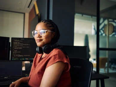 Young woman programmer focused on her work, coding on dual monitors in a modern office environment