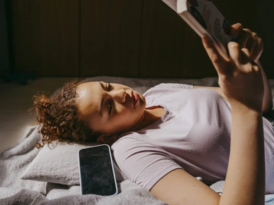 Teenage girl reading book while lying on bed