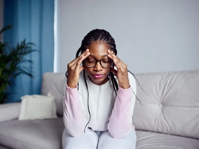 A young girl is sitting on the couch at home with her head in her hands.